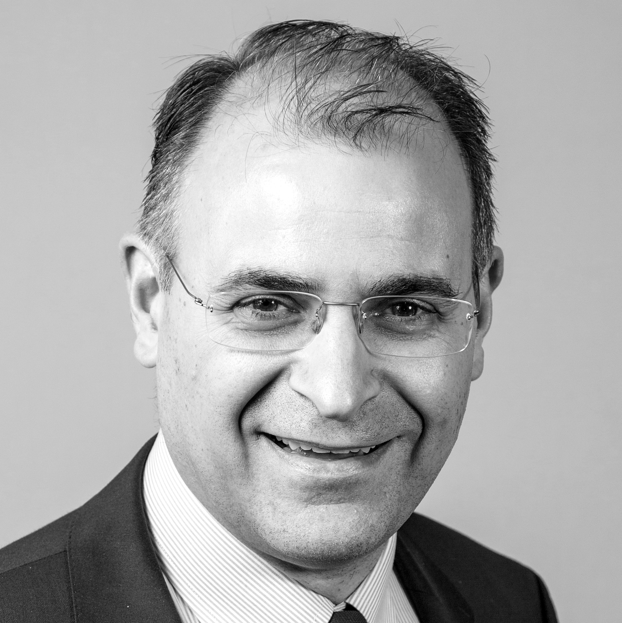 Black and white photograph of the head and shoulders of a middle-aged man with thinning hair and frameless glasses. The man is smiling and looking straight at the camera.