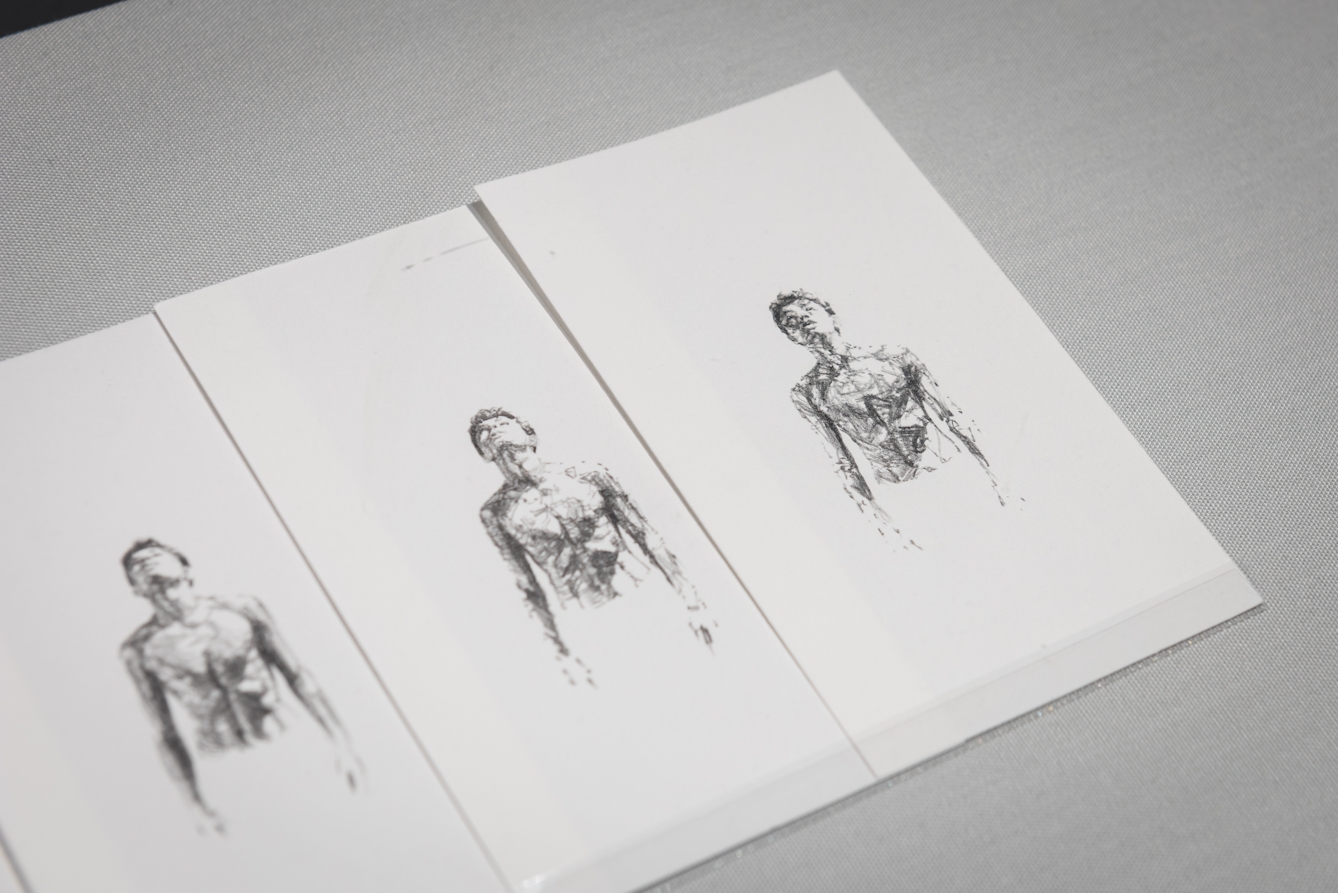 Colour photograph of three sketches on white paper. The sketches show the shirtless upper body, specifically the torso, chest and head, of a slim boy. In all the sketches the boy is shown looking upwards  .