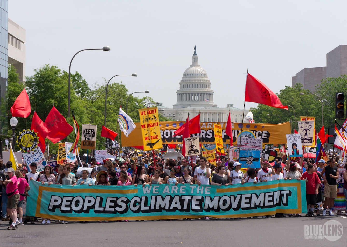 Lots of people holding brightly coloured banners and flags on a climate change march in Washington, with the Capitol building in the background.