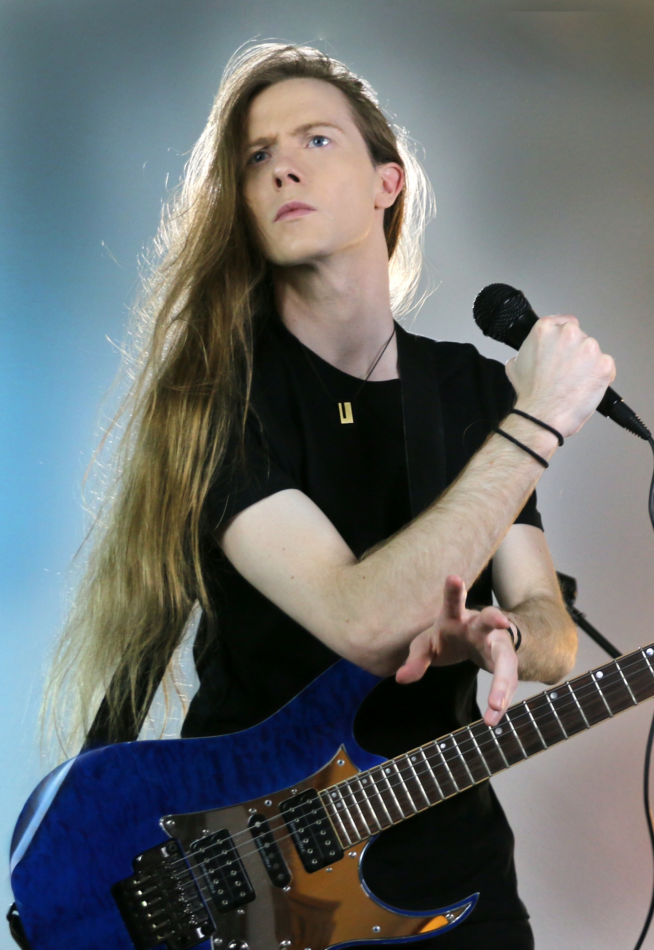 Photo of man with long hair holding a microphone and a guitar.