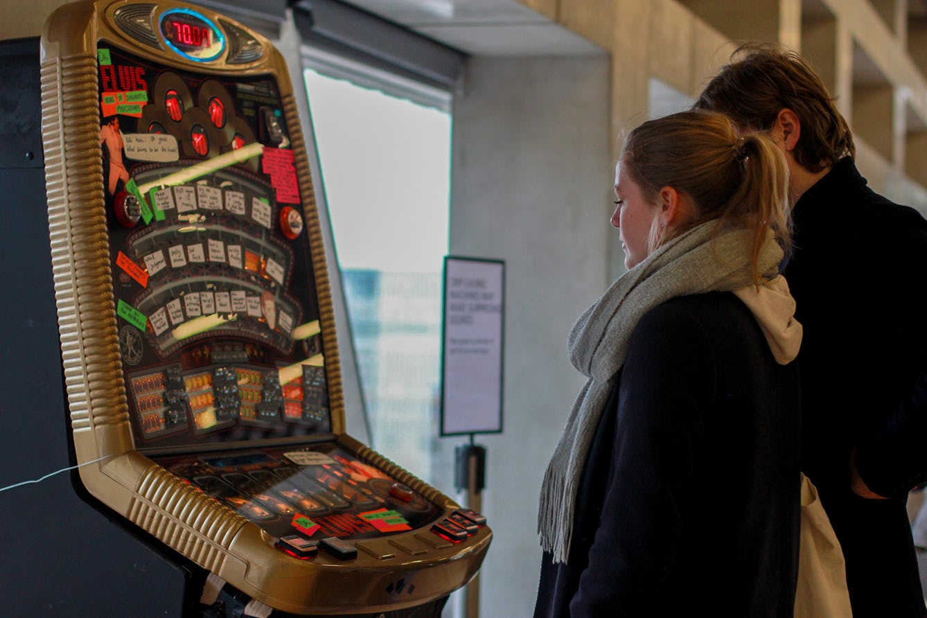 Two people standing in front of a DIY hacked Crip Casino fruit machine.