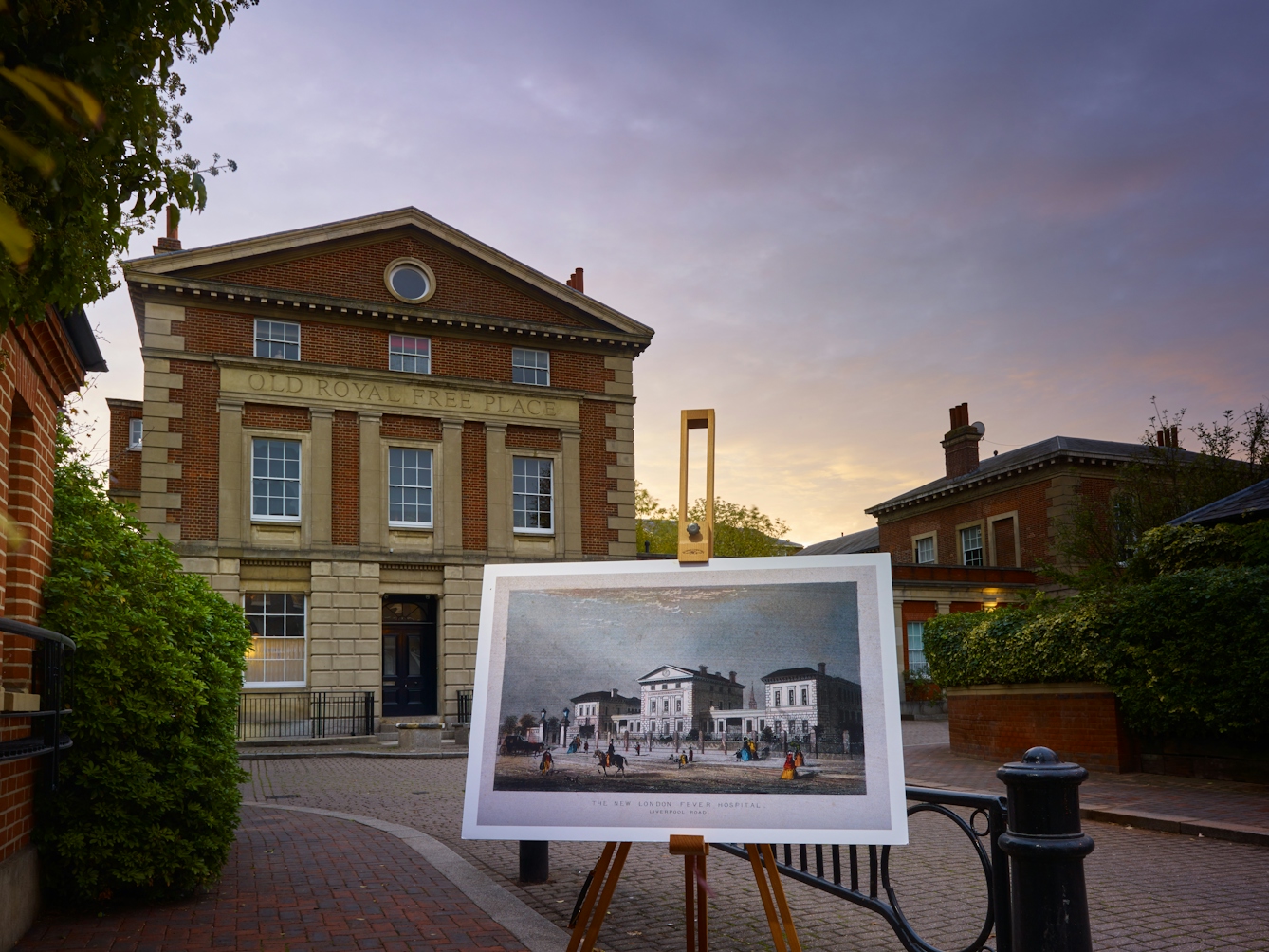 Photograph of the former New London Fever Hospital with an historical image of the hospital displayed in front of it on a wooden artist's easel.