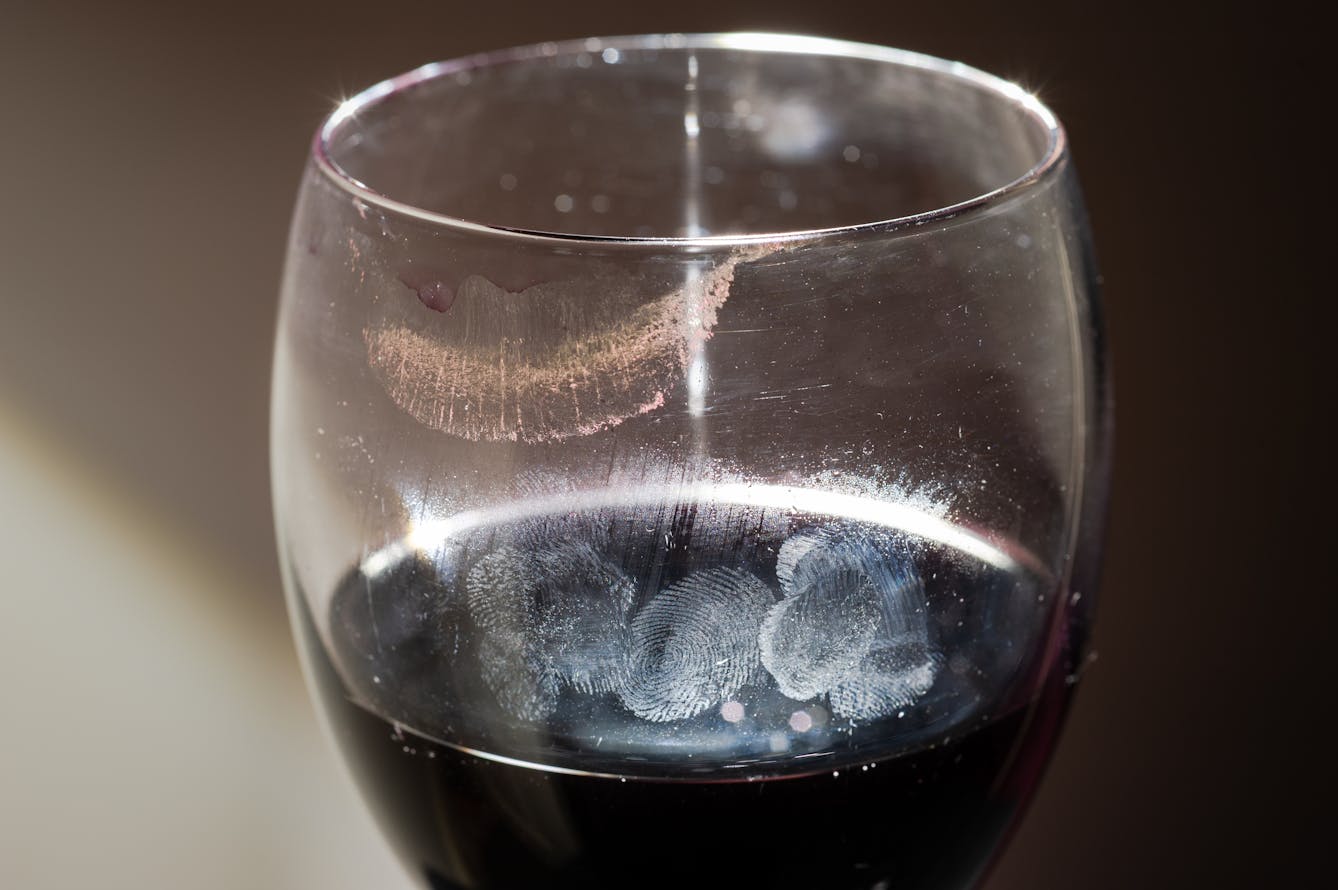 Photograph of wine glass containing red wine. on the surface and around the lip of the glass are lipstick and finger print marks.