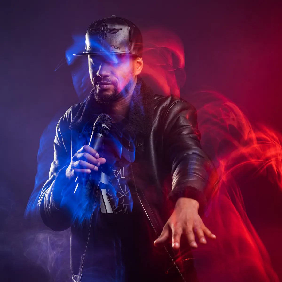 A male rap artist dressed in a black leather hat and jacket is holding a microphone, dancing with his arm outstretched in front of him. The room is filled with smoke and blue and red lighting effects highlight his movement.