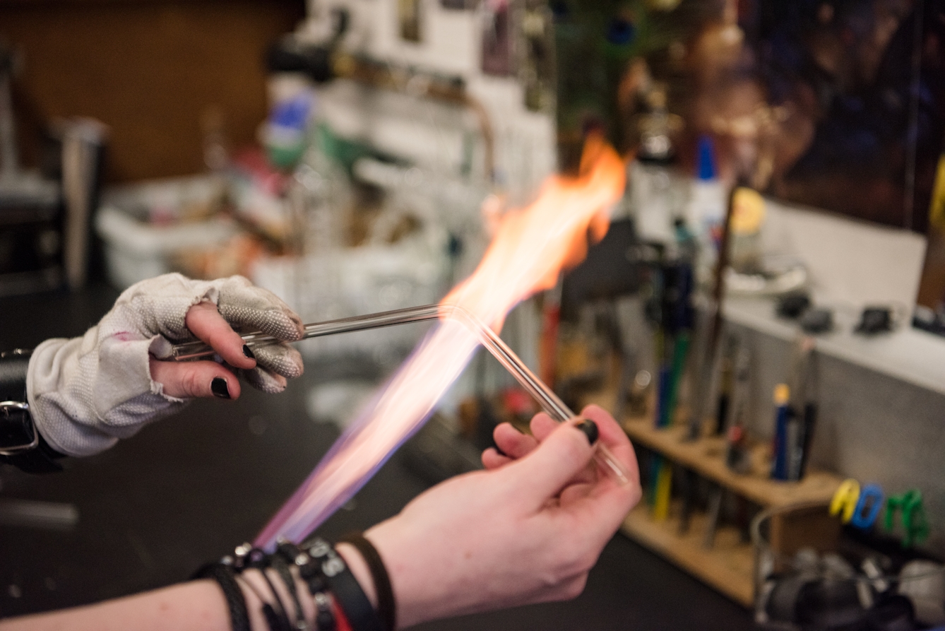 Hands holding a glass rod over a flame, bending it into an obtuse angle.