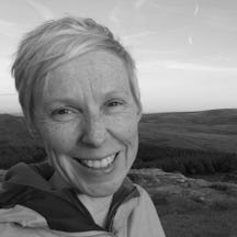 Head and shoulders photo of a woman with short, fair hair, against a background of hills and fields.