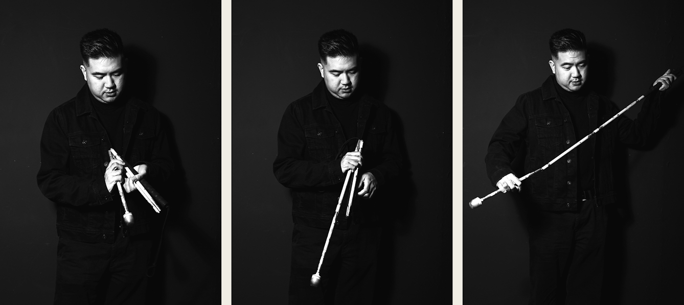 Photographic black and white triptych. The 3 images show a man standing against a dark grey wall holding a white cane in his hands. He is looking down towards the cane in his hands. Each image the cane being unfolded, from completely folded in the first image to completely assembled in the last.