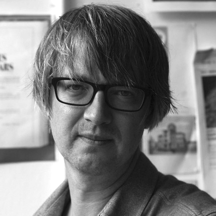Head and shoulders photograph of a man with mid-length hair and dark-rimmed glasses.
