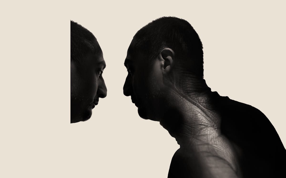 Photographic portrait of a man's head and shoulders in profile, looking to the left. He is pictured in silhouette against a cream background. Overlaid onto his neck and shoulders is an image of a scar, showing the texture of the skin and the scar tissue. The man's face is looking at a reflection of himself as if in a mirror although his reflection is cut off so only half of this head can be seen.