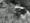 Black and white still from a film showing a man diving from a grassy area into a pond.
