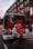 A photograph from July 2000, in which a drag queen wearing red stands in front of a bus. The number "28" has been painted in red, dripping paint onto the windscreen of the bus.