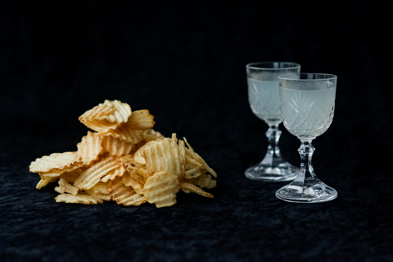 Photograph of a pile of crisps on the left and two crystal cut glasses containing lemonade on the right. The background is a black velvet material.