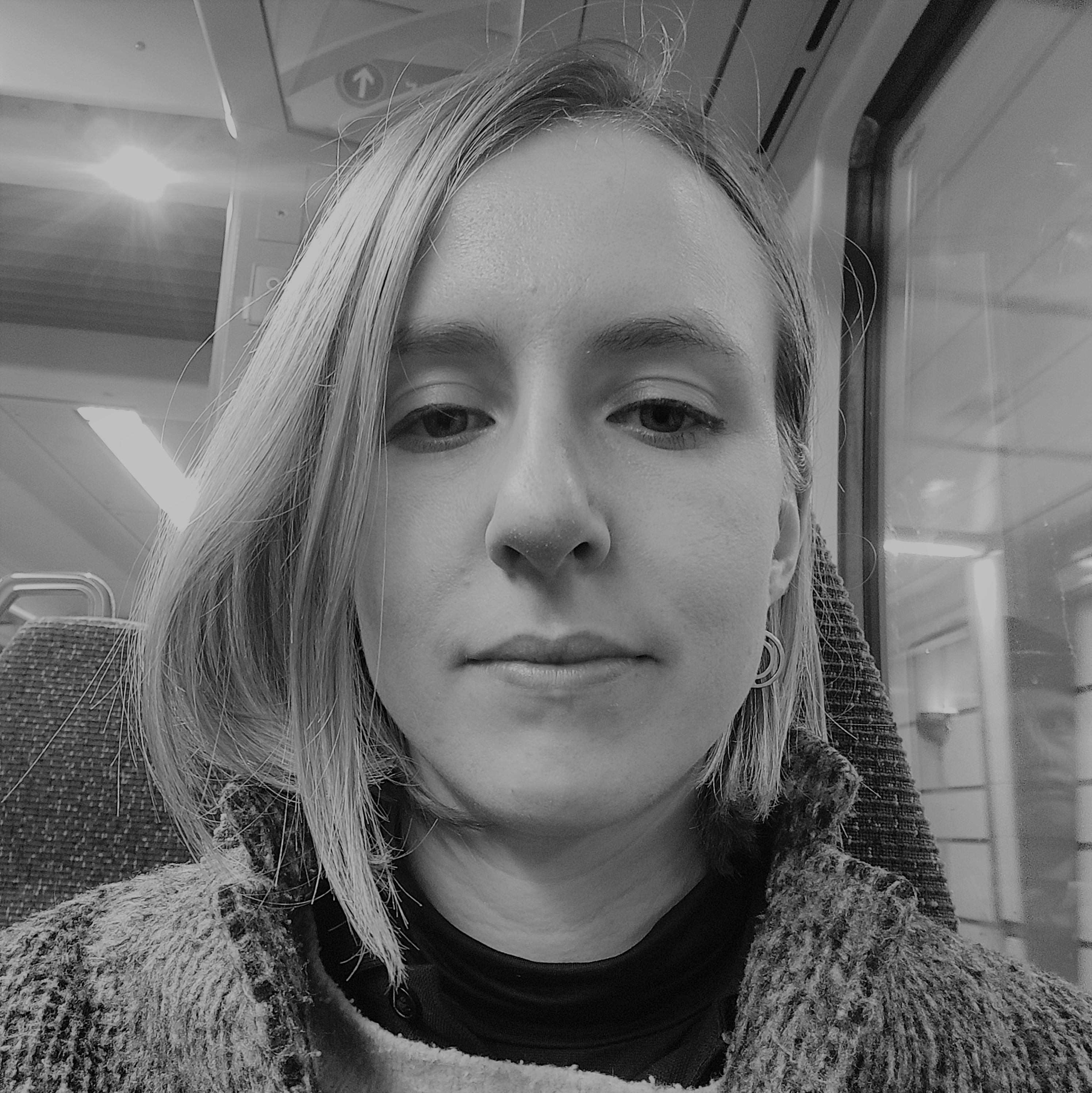 Head and shoulders photograph of a woman on a train, with neck-length hair, falling forward over her right cheek 