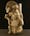 Photograph of a ceramic sculpture of a warrior, kneeling on left knee, bearing square shield on left arm and massive club in right hand. Wears elaborate helmet with crosswise crest, crescentic blade and two mushroom knobs.