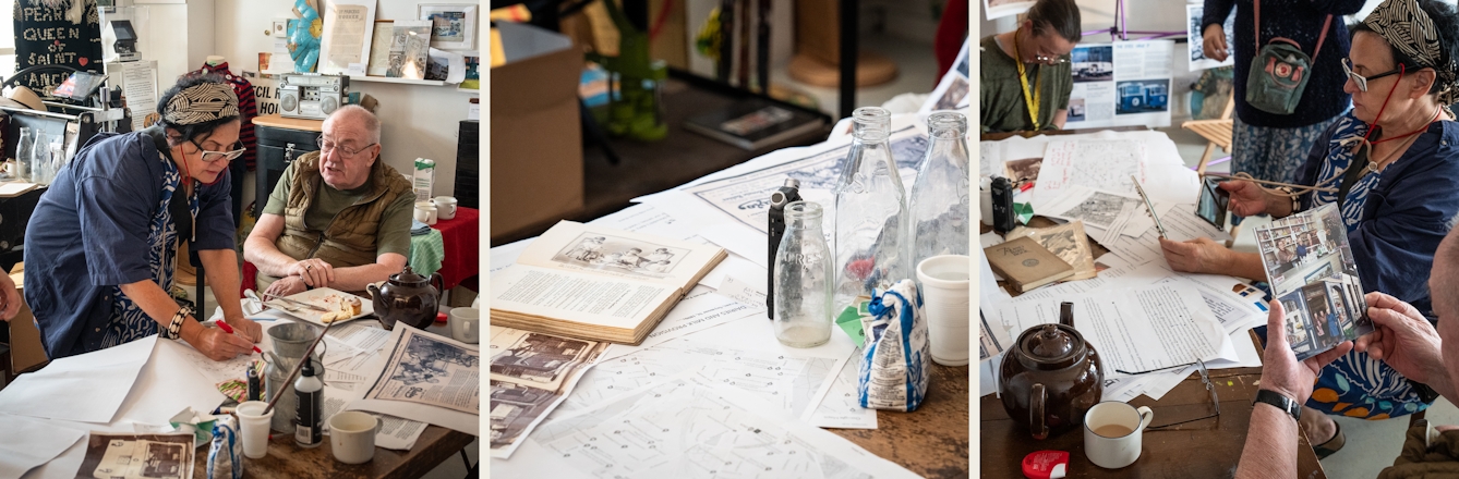Photographic triptych of square photographs showing a workshop taking place in a community space. The left image shows a man sat at a table covered in paper and a tea pot, talking to a woman who is in the process of writing on a piece of paper. The centre image shows a section of the tabletop, covered in printed maps, open boos and empty glass milk bottles. The image on the right shows a man holding a couple of old colour photographs in his hands. In the background is a table covered in papers and people sat around in the process of working.