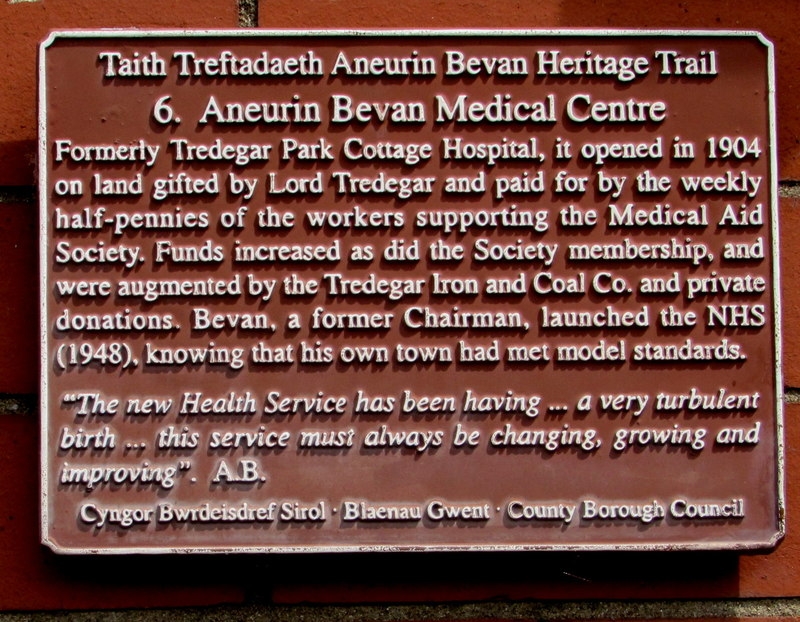 Photograph of the commemorative plaque that forms part of the Taith Treftadaeth Aneurin Bevan Heritage Trail. Plaque reads: "Aneurin Bevan Medical Centre. Formerly Tredegar Park Cottage Hospital, it opened in 1904 on land gifted by Lord Tredegar and paid for by the weekly half-pennies of the workers supporting the Medical Aid Society. Funds increased as did the Society membership, and were augmented by the Tredegar Iron and Coal Co. and private donations. Bevan, a former Chairman, launched the NHS (1948), knowing that his own town had met model standards. 'The new Health Service has been having ... a very turbulent birth ... this service must always be changing, growing and improving.' A.B."