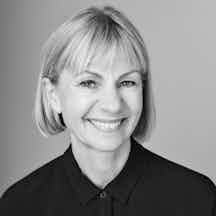 Black and white head and shoulders portrait of Kate Mosse who has a short-cropped blonde bob and is wearing a black shirt.