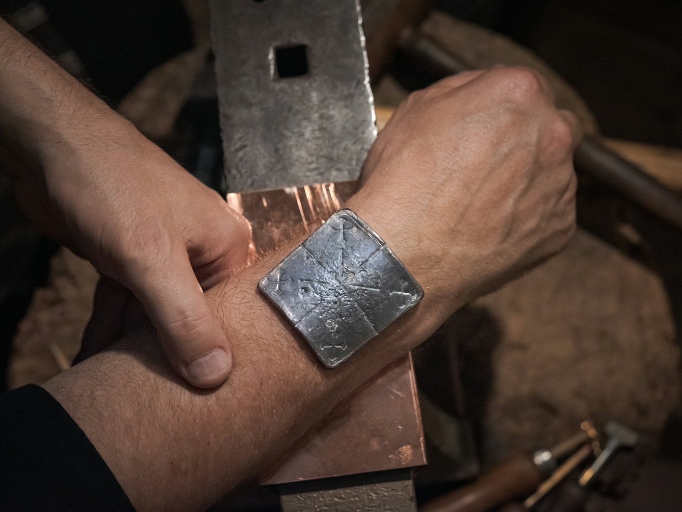Photograph of the lead healing plate placed on the wrist of a man. The wrist is resting on an anvil. Inscribed on the lead plate are five crosses, representing the five wounds of Christ.