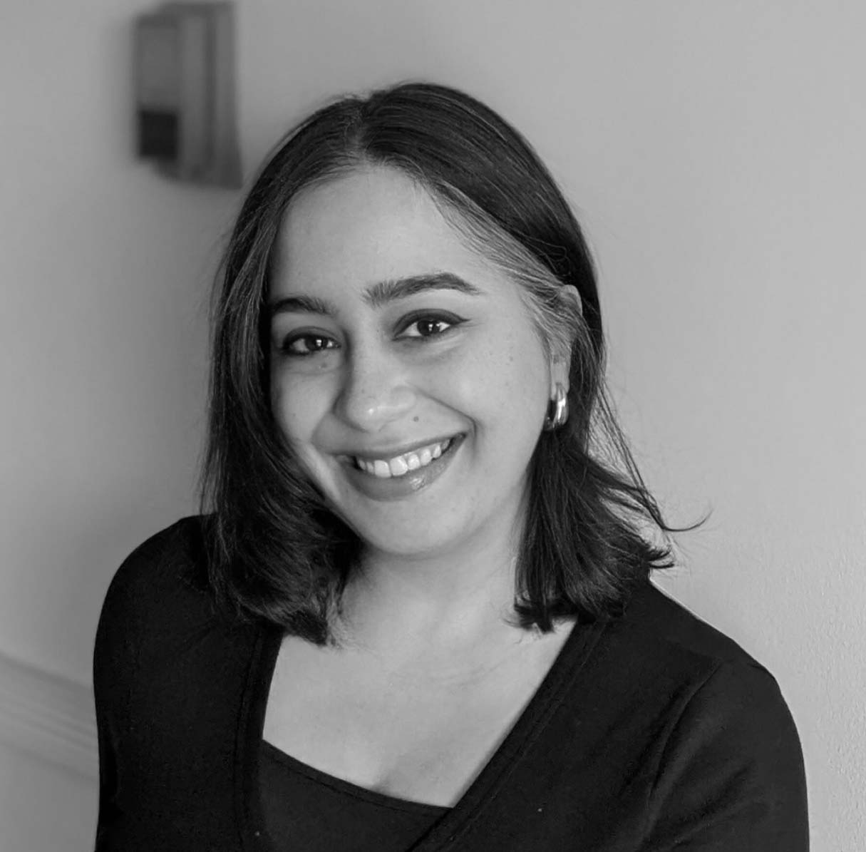 Black and white photograph of the head and shoulders of a woman with shoulder length dark hair.  The woman is smiling and looking directly at the camera.
