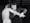 Black and white still from a film showing a man in a suit manipulating the right arm of an almost naked man.