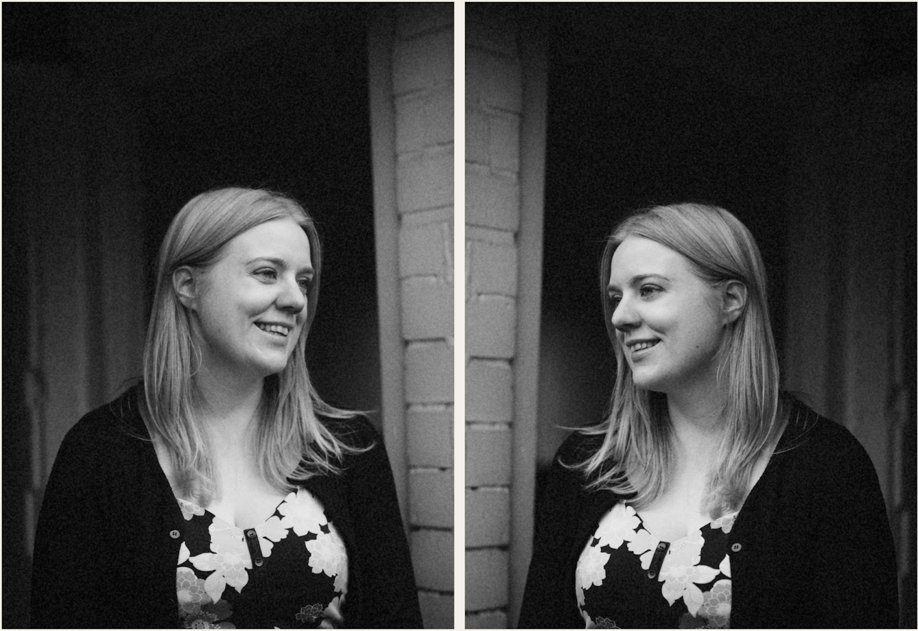 Photographic black and white diptych. The images both show the same young woman with blond hair, wearing a floral dress and black cardigan, standing outside a front door and white brickwork. In each image she is pictured in profile, looking towards herself in the other image, as if in a mirror. In both images the woman is smiling.