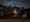 Photograph of Garston Spiritualist Church, Watford, at night. Set in a residential setting the double doors of the church are lit by a porch light, which is also spilling into the small yard. The church is partially hidden by a brick wall come gate, and two bushes.