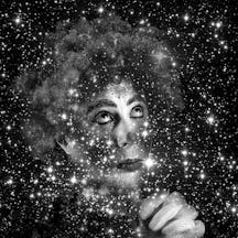 Black and white portrait of the artist Eduardo Navarro dressed in clown makeup and costume with hands clasped and looking upwards as if in prayer. The image is superimposed on an astronomical background of stars and galaxies.