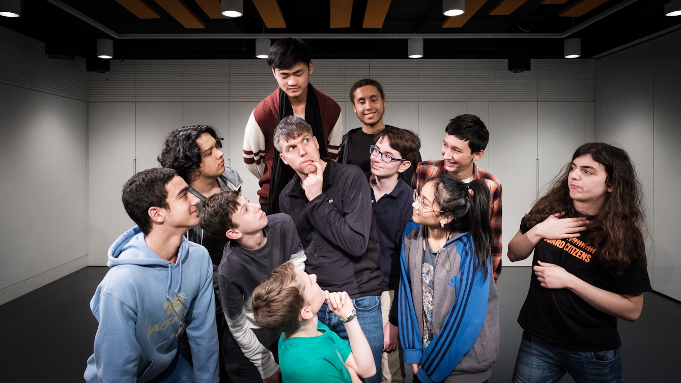 Photograph of ten of the RawMinds Improv Comedy youth group surrounding and looking at science comedian, Simon Watt who is centre frame. 