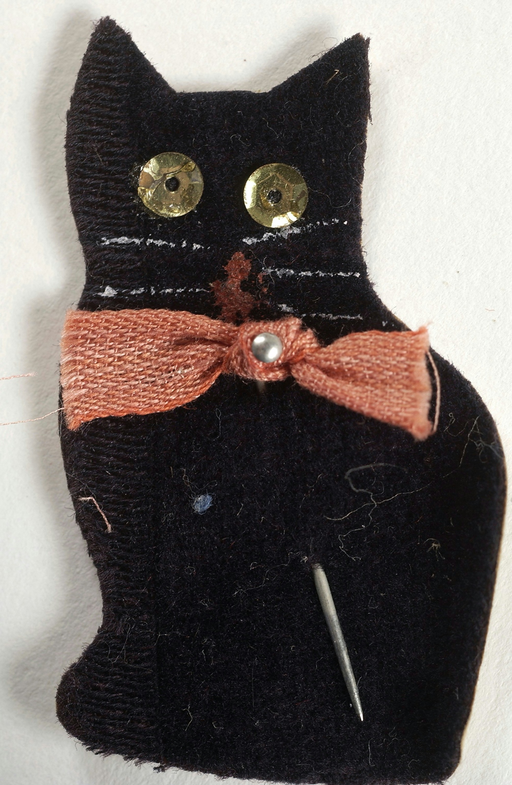 A cat handmade from black fabric, with gold sequins for eyes, and wearing a large pink-red bow on its neck.