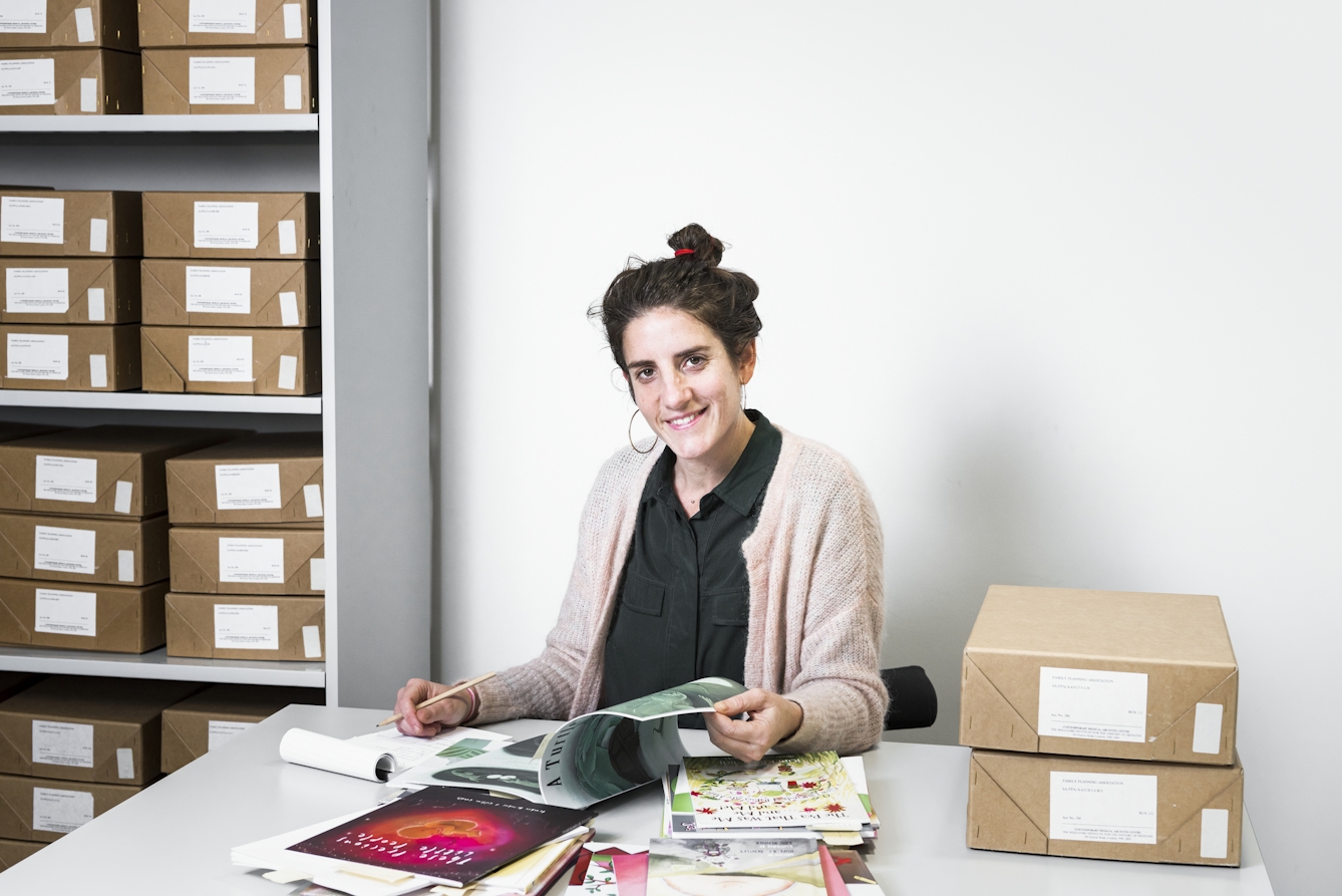 Dr Sigrid Vertommen seated in Wellcome Library with archive boxes and a selection of documents and publications from an archive collection