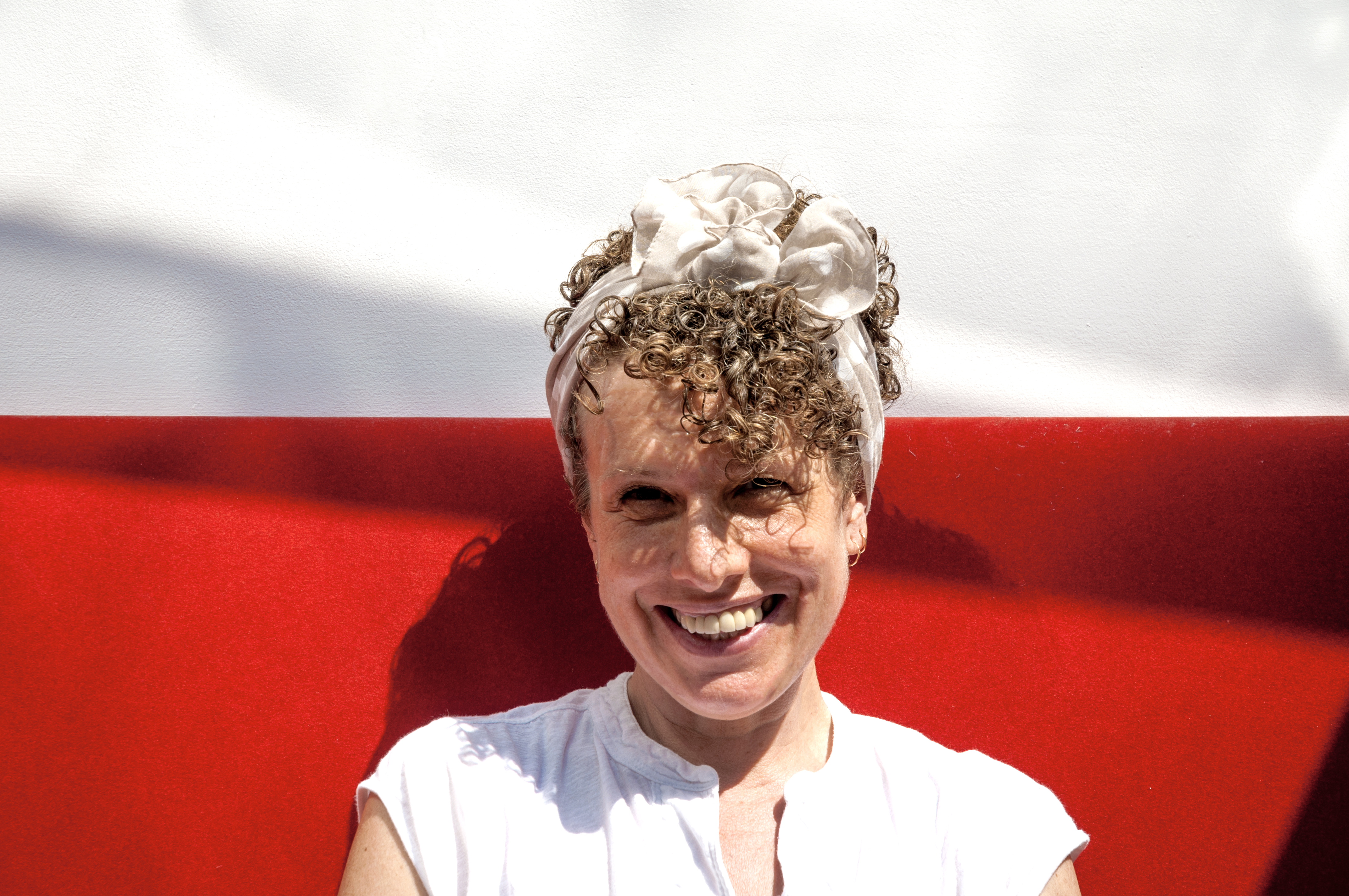 Headshot of Naomi Woddis smiling in front of a white and red background.