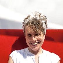 Headshot of Naomi Woddis smiling in front of a white and red background.