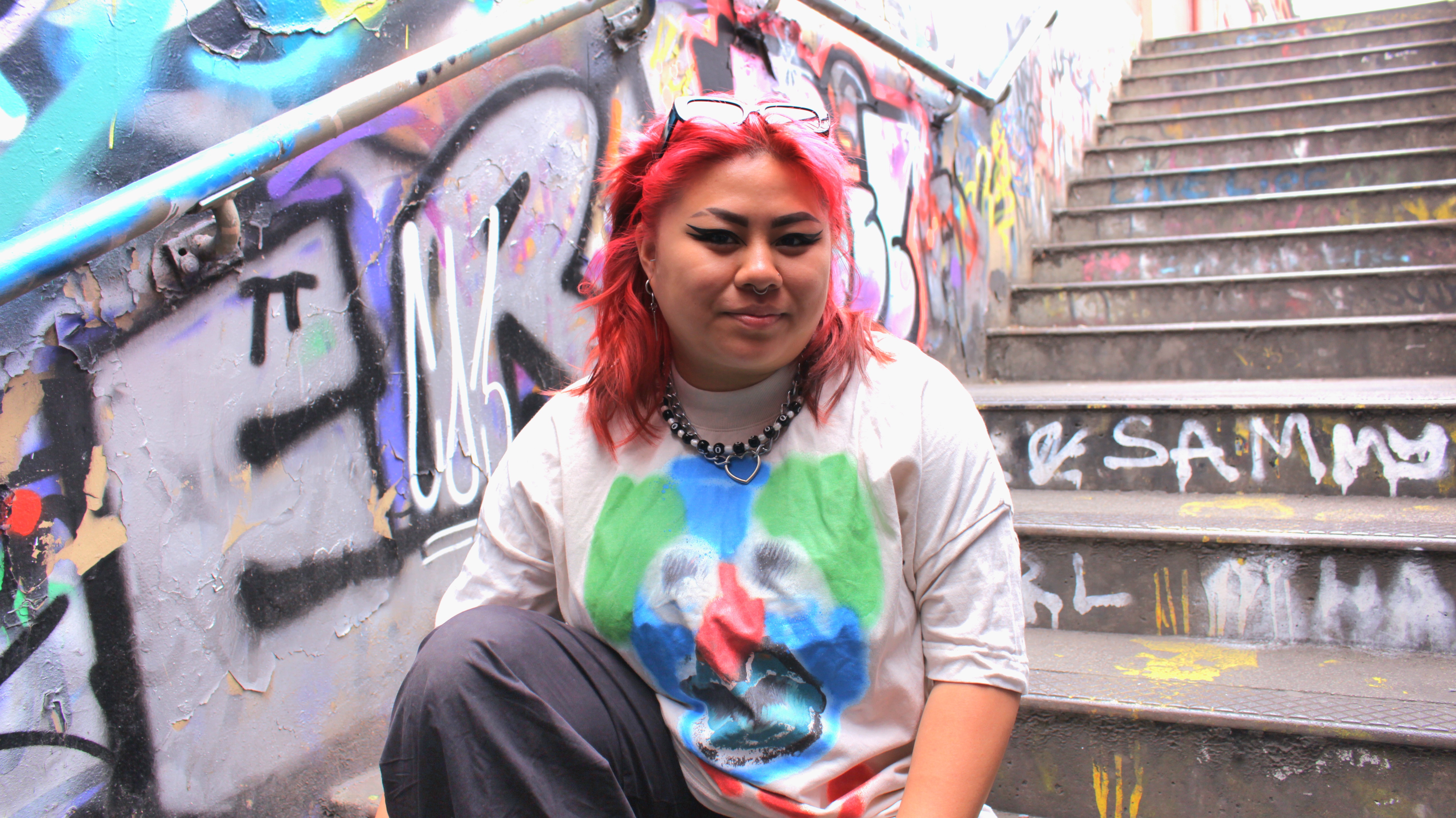 A photo of Boe sitting outside on stairs, with graffiti in the background 