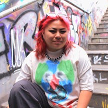 A photo of Boe sitting outside on stairs, with graffiti in the background 