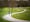 Photograph of a large robot walking and talking with a young boy in school uniform who's holding a football, down a winding path in the park.