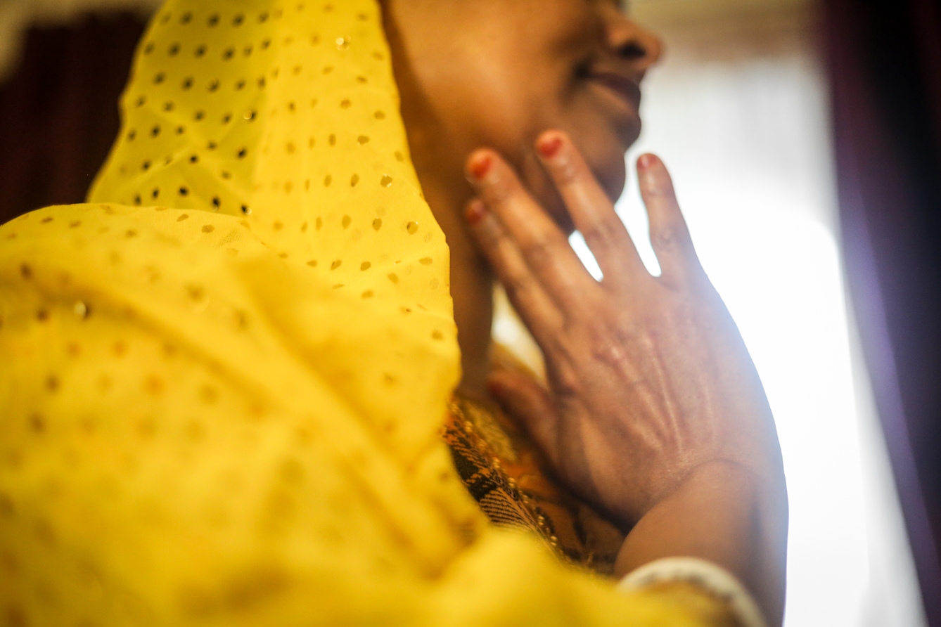 Photograph of a woman's hand against her chin, taken with a very shallow depth of field such that most of the image is out of focus. You can only see the woman's mouth and nose. She is wearing a yellow shawl.
