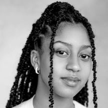 Black and white photograph of the head and shoulders of a young black woman with long plaited hair. She is looking straight at the camera and smiling.