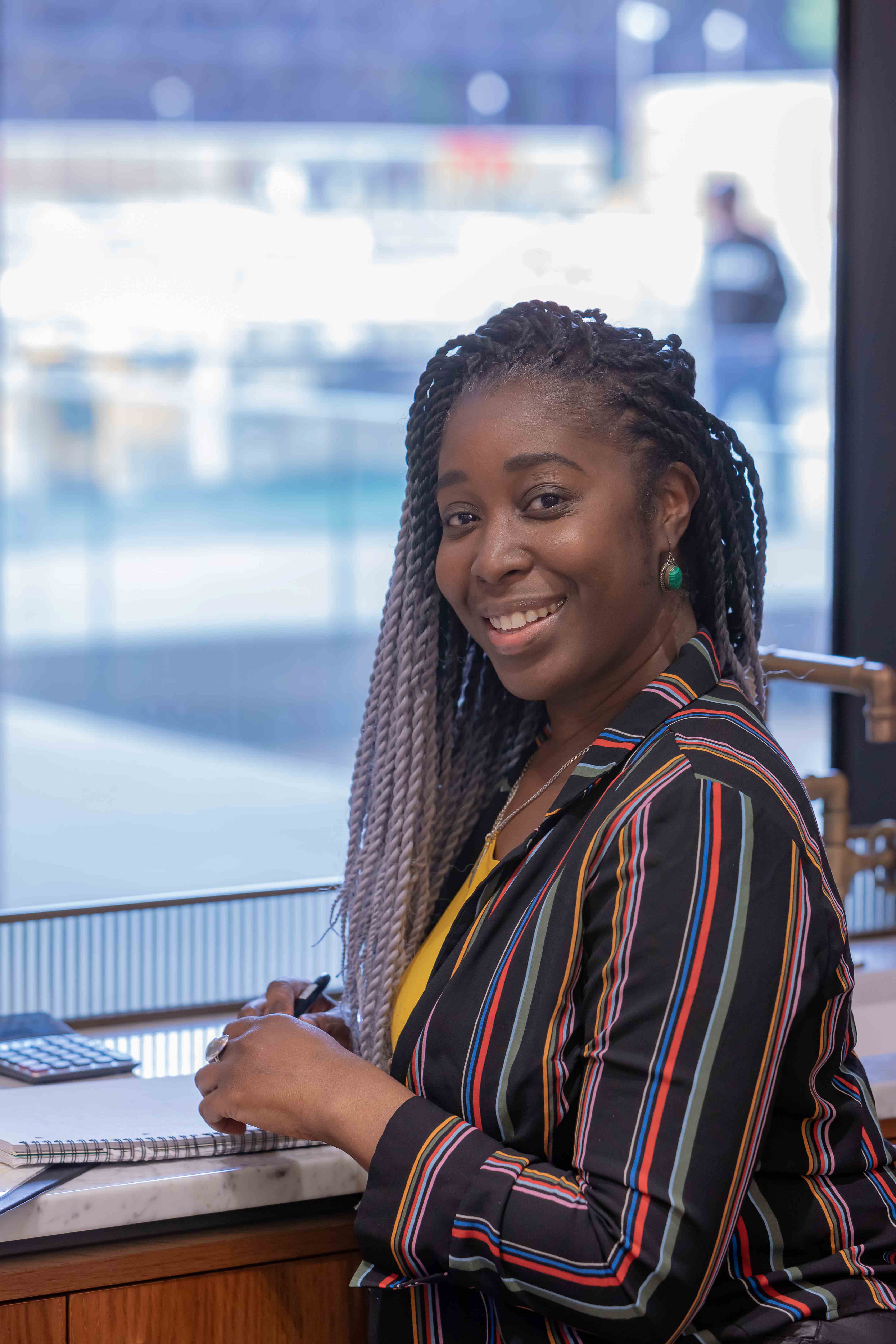 A headshot of Sasha smiling and sitting at a desk with a notebook
