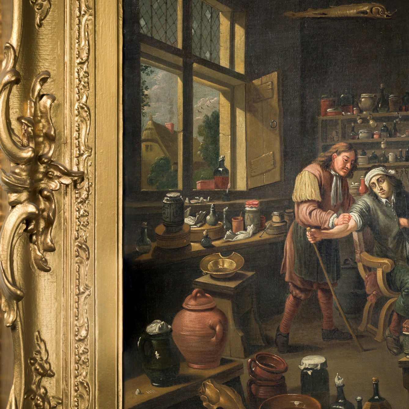 Photograph of a section of an oil painting in a gilded ornate frame, against a brick wall painted white. The oil painting shows a man letting blood from another seated man's arm. Beside them stands a woman holding a bucket. Waiting dates from 1610 to 1690.