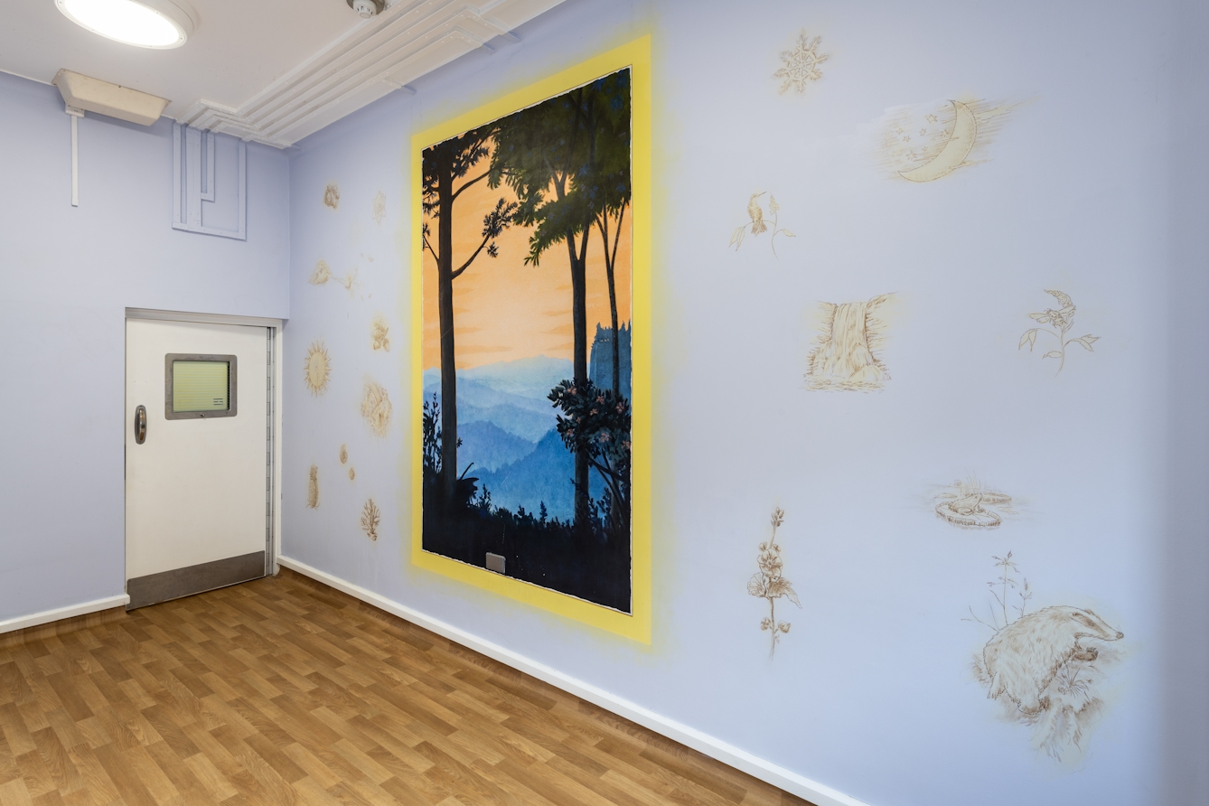 A photograph showing a room with a wood laminate floor, with a white door in which there is a small square glass window.  The walls are a light blue decorated with light gold looking textured prints of things such as suns, clouds, and shells each no bigger than 30 centimeters scattered across it. On the blue background there is a bright lemon yellow border in portrait orientation. Within the border there is a black silhouette of two trees with long trunks, one on the left and one on the right. They appear in the foreground together with silhouetted grass at the bottom of the frame. In the distance, different tones of blue make up a range of mountains and hills below. Above the hills, there is a light orange sky.  