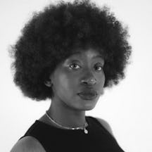 Head and shoulders photograph of a woman with afro hair, wearing a sleeveless dress and a necklace.