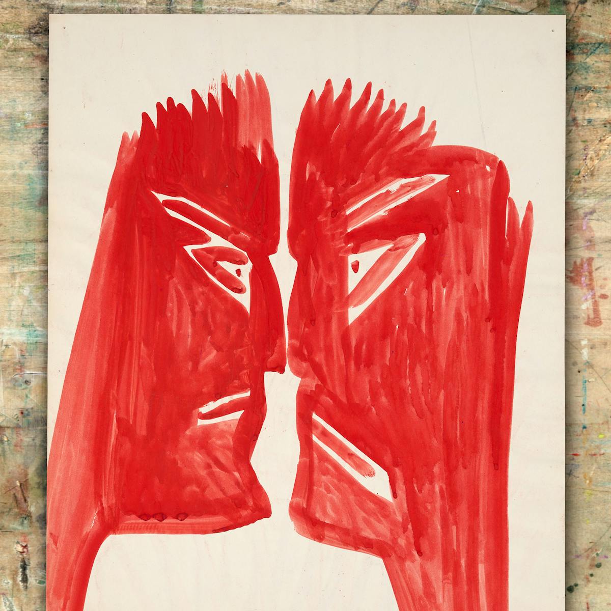 Image of a watercolour artwork resting on a paint splattered wooden artist's board. The watercolour artwork shows two faces in profile, staring at each other, nose to nose. Each face is painted solely in red and the expression on both is one of anger.
