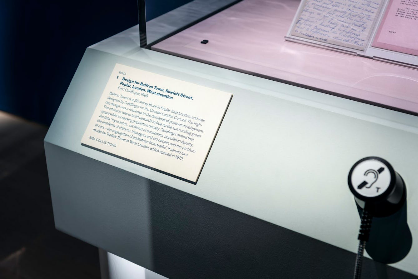 Image of a text label and a sound handset mounted on an object display case in the Living with Buildings exhibition. The label is mounted at an angle. The sound handset includes the induction loop symbol.