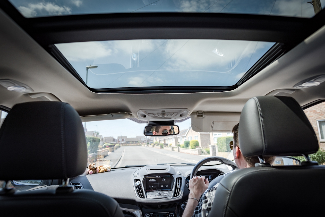 Photograph from the back seat of a car of a man driving down a residential street.