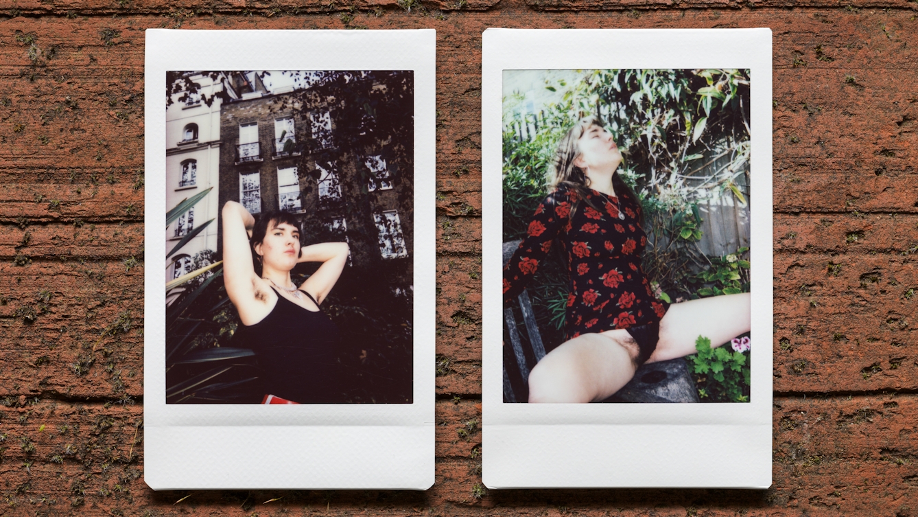 Photograph of two Instax Mini instant film prints in a line, resting on a textured brick surface. The two prints feature the same woman. The print on the left shows the her nestled within the branches and leaves of a tree outside a tall row of houses, with her arms raised up to show her armpit hair. The print on the right shows the same woman sitting in a garden scene with her clothes pulled up and her legs apart showing her black knickers and pubic hair.