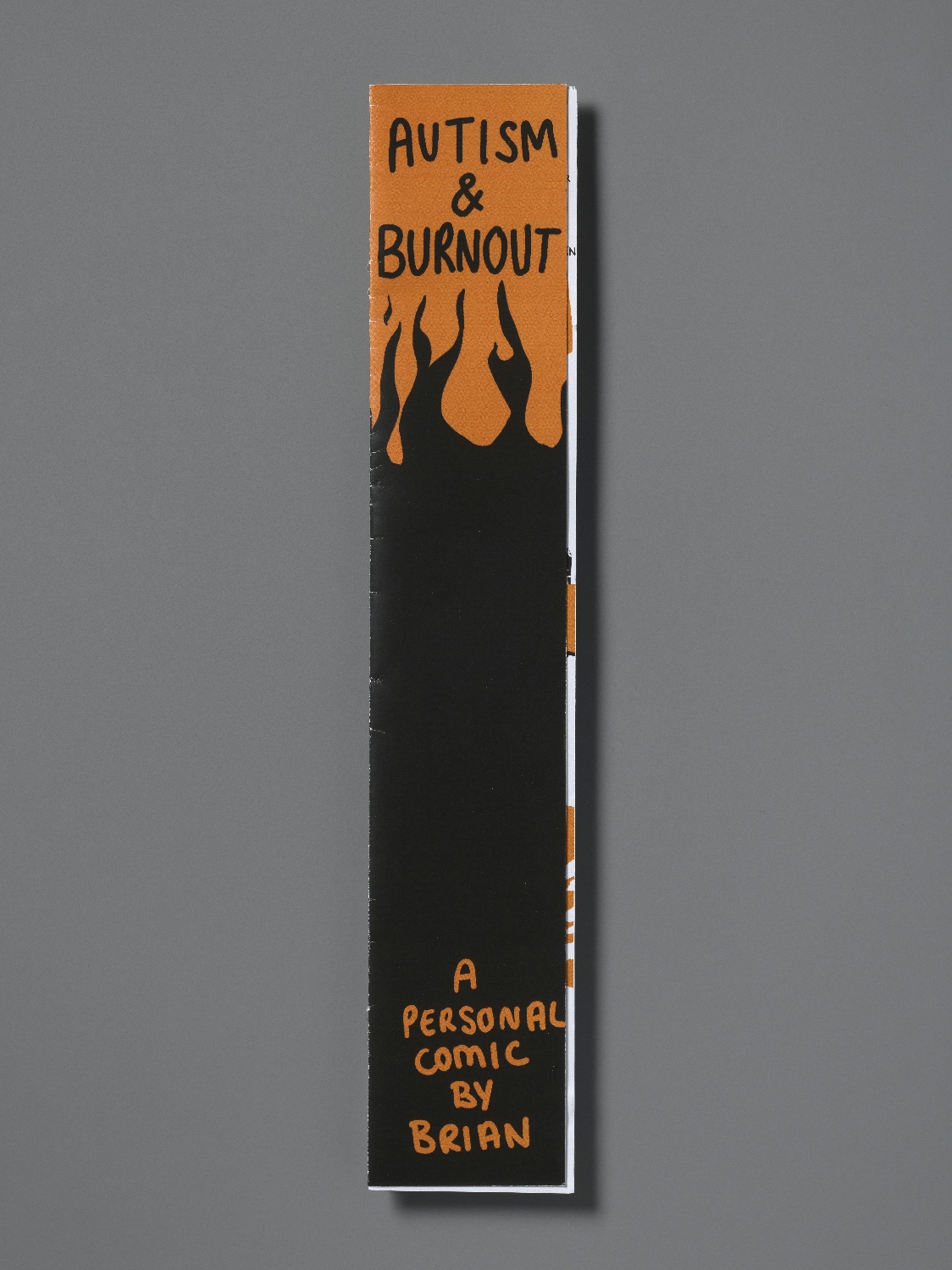 Front cover of a per-zine called Autism and Burnout. The zine consists of a long narrow strip of paper folded into pages. The cover has an orange background with black flames dancing below the title. In the black area is written "A personal comic by Brian Tyrrell" in orange.