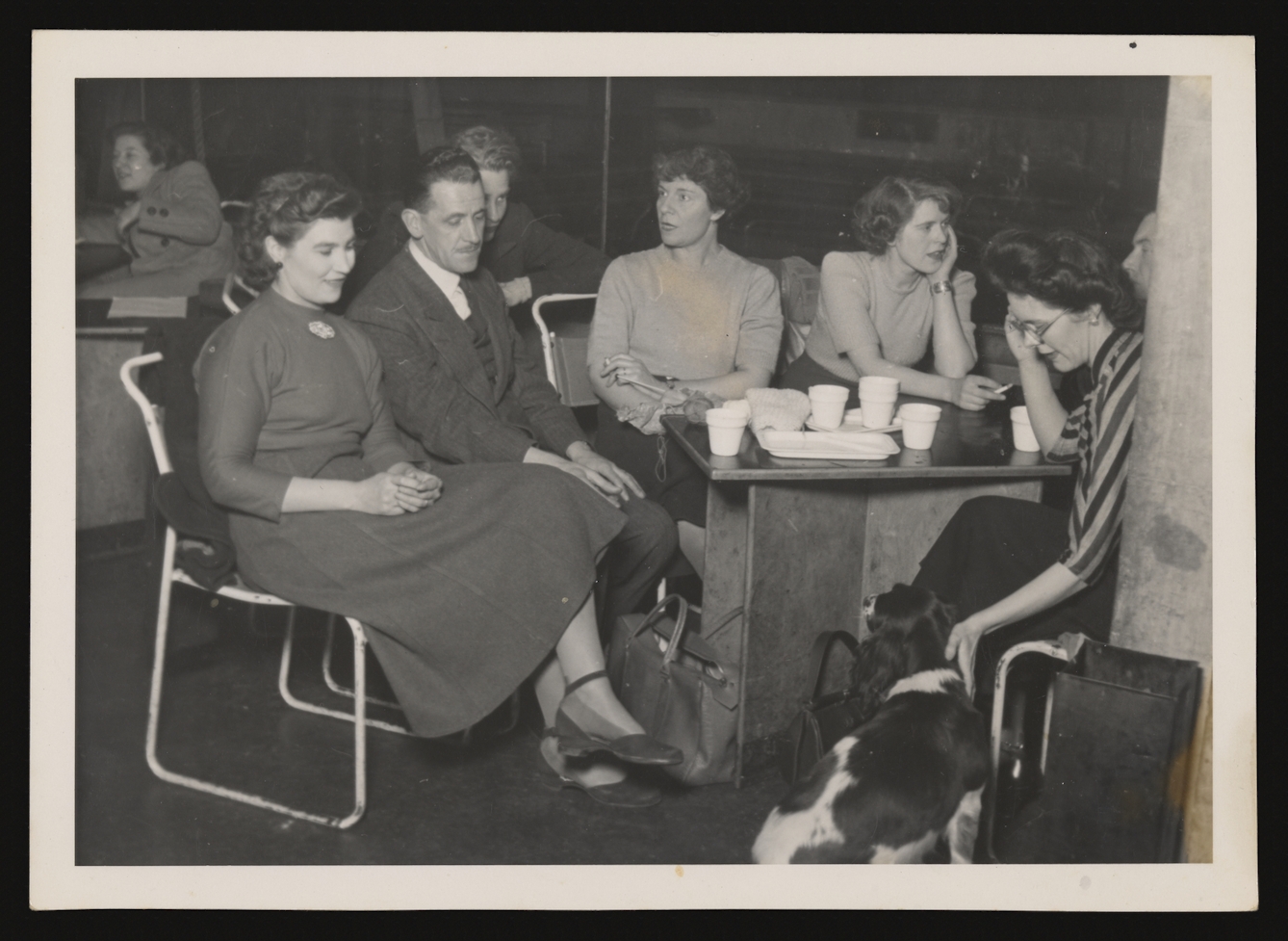 Black and white photograph showing a group of young men and women sitting around a table.