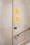 A photograph showing wayfinding signs in the Wellcome Collection building. There are two yellow circular stickers on a light grey marble wall. Both stickers have blue writing and an arrow pointing upwards. The top sticker reads 'Reading Room' and the one below reads 'Library'. Below the sticker signage is a lightswitch and a stair railing.