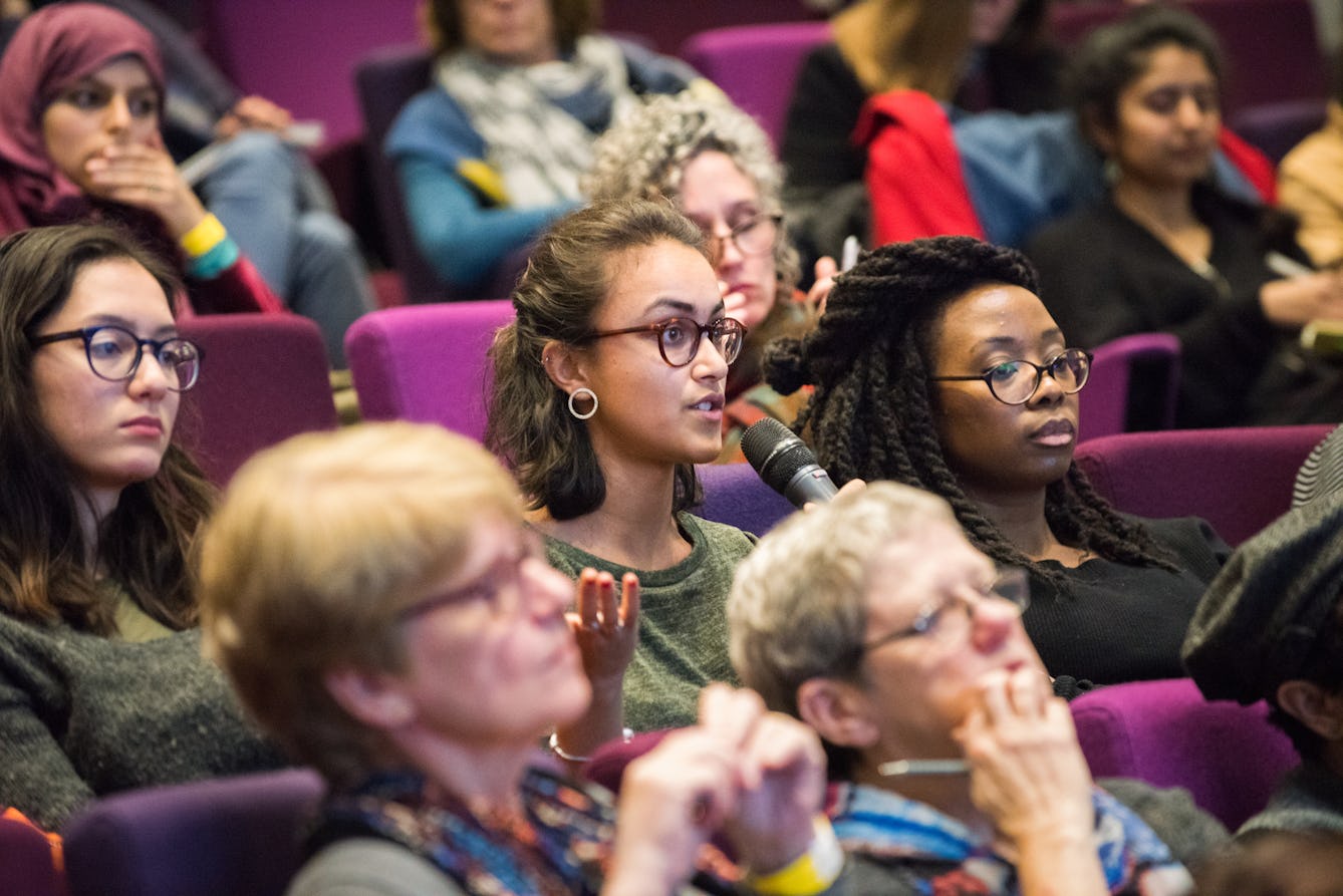 People sitting in rows of purple seating in the auditorium at Wellcome Collection, a member of the audience is speaking into a handheld microphone and gesturing with their other hand.