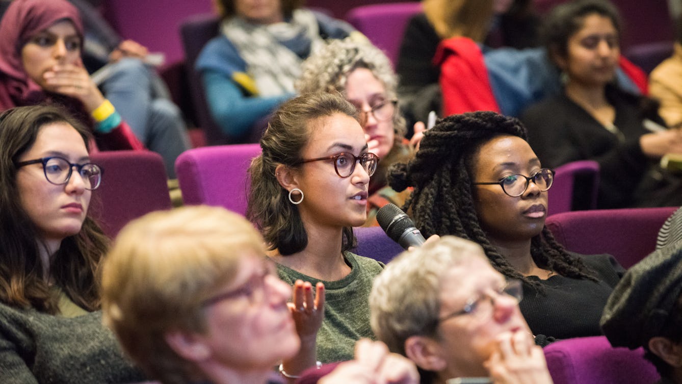 People sitting in rows of purple seating in the auditorium at Wellcome Collection, a member of the audience is speaking into a handheld microphone and gesturing with their other hand.